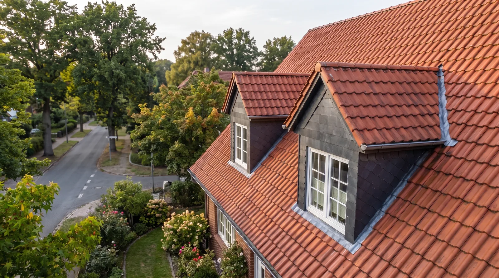 Steildach mit roten Hohlpfannen und zwei Giebelgauben, deren Wangen mit dunklem Schiefer verkleidet sind, sichtbarer Blei-Anschluss zur Hauptdachfläche